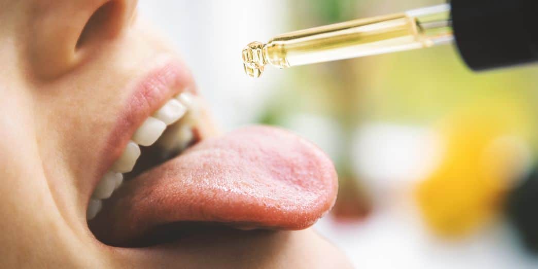 una persona usando cbd aceite y colocar gotas debajo de la lengua. Este es el preferido cbd método de entrega cuando se usan aceites.