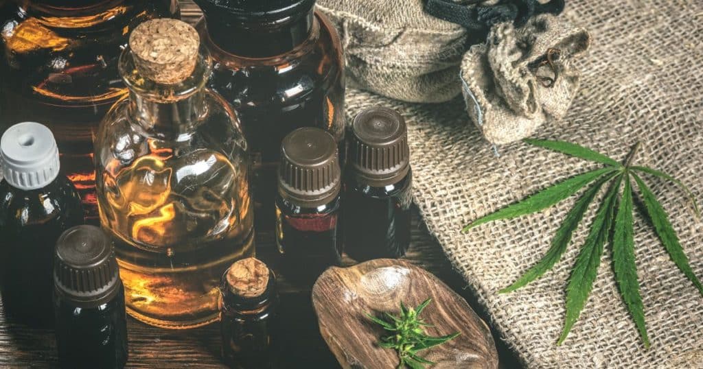 a collection of CBD oils on a table. The oils are unlabeled and all sitting next to a cannabis leaf. The picture is to give context to what CBD oil is in general so the reader will have a more comprehensive understanding of how it will relate to hair growth and hair loss in the article.