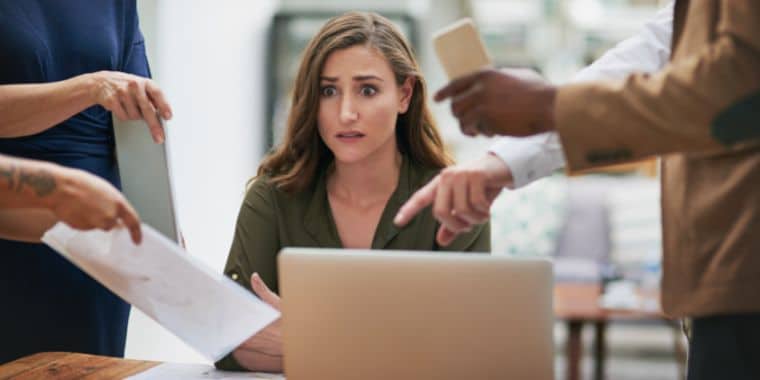 een vrouw die erg gestrest is van angst. Ze zit in een kantoor met veel collega's die over haar kijken