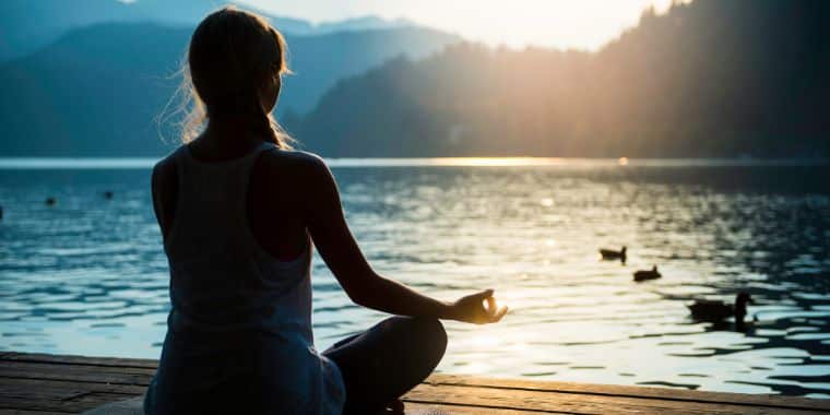a woman meditating in front of a lake