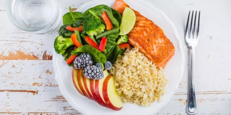 ein Teller mit gesunden Lebensmitteln wie Lachs und Naturreis und Apfelscheiben.